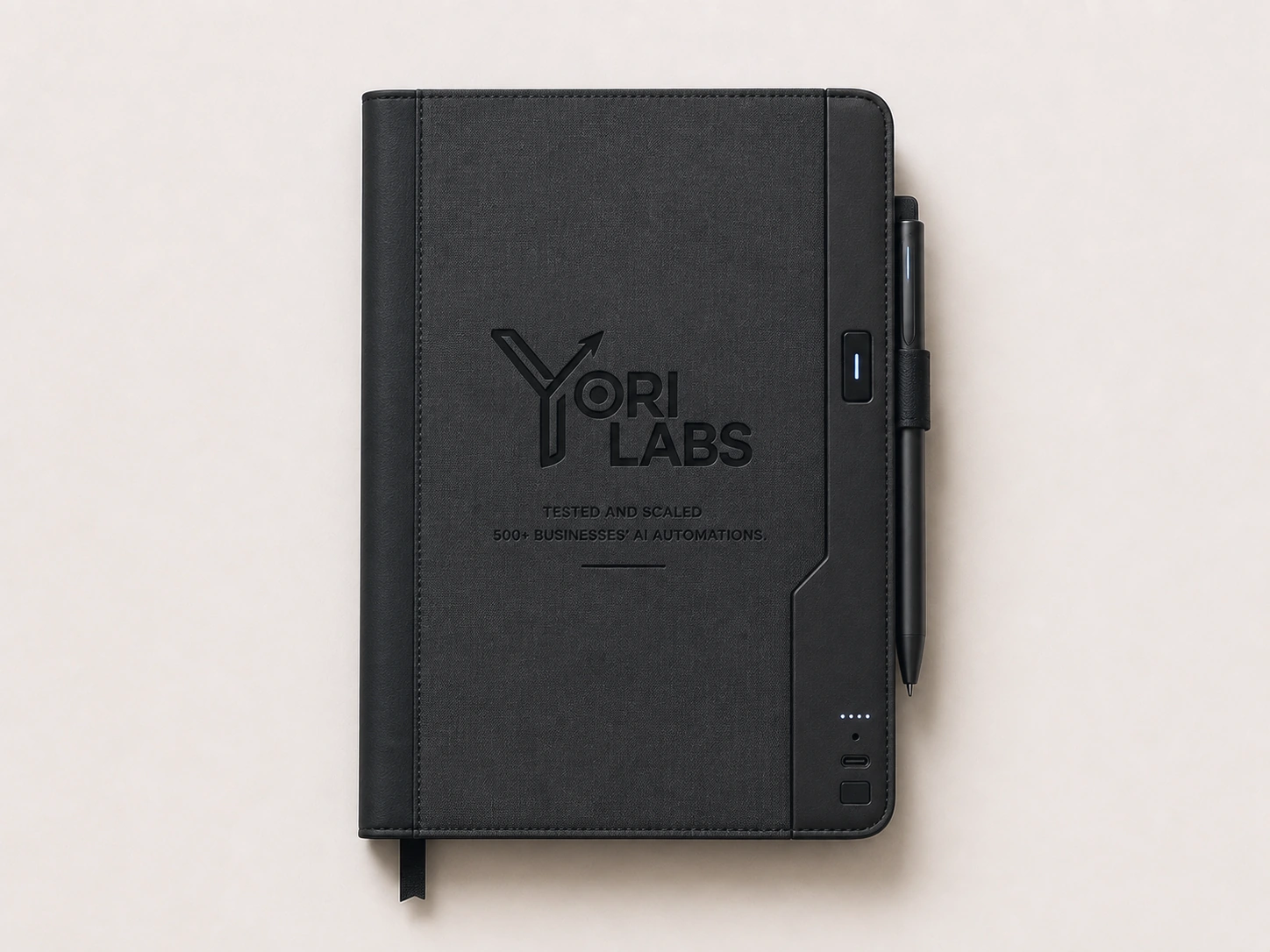 The Yori Labs notebook closed: a matte black cover embossed with the logo, a pen clipped to its spine, tested and scaled by 500+ businesses' AI automations